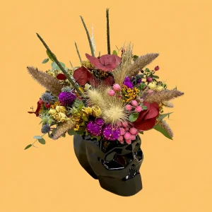 Esencia de Catrina, calavera de cerámica negra con flores y follajes preservados en tonos morados, rosas, amarillos y rojizos.