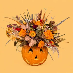 Floral Pumpkin, calabaza natural con rostro tallado, flores naranjas y follajes frescos y preservados en tonos de temporada.