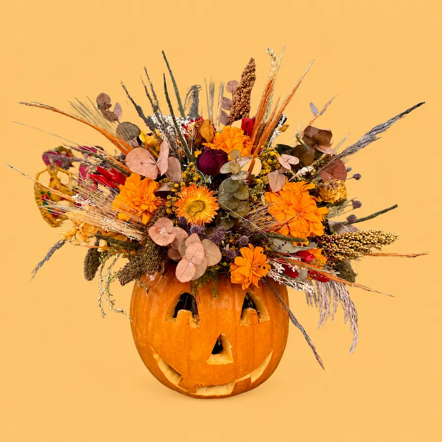 Floral Pumpkin, calabaza natural con rostro tallado, flores naranjas y follajes frescos y preservados en tonos de temporada.